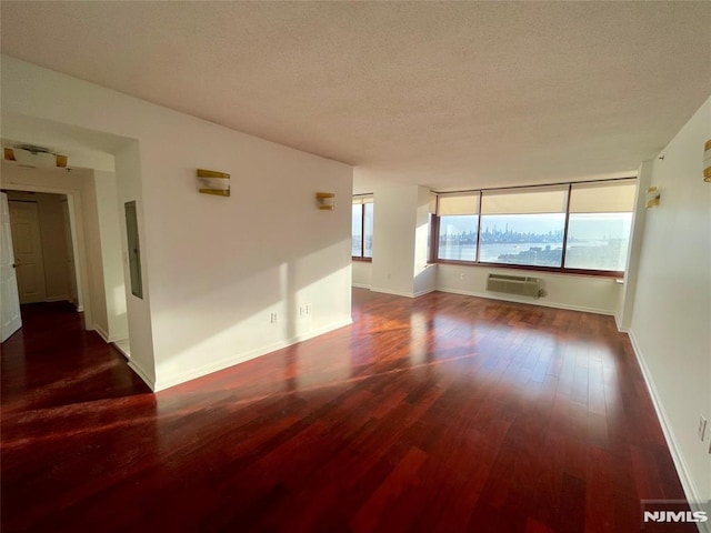 empty room featuring a textured ceiling, a water view, an AC wall unit, and dark wood-type flooring