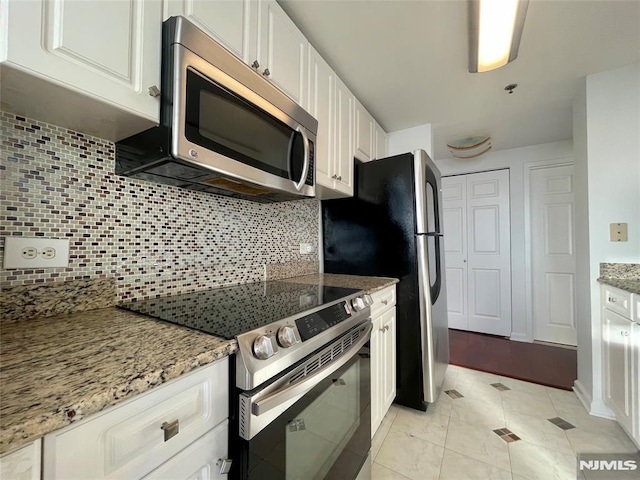 kitchen featuring light stone countertops, appliances with stainless steel finishes, backsplash, light tile patterned floors, and white cabinetry