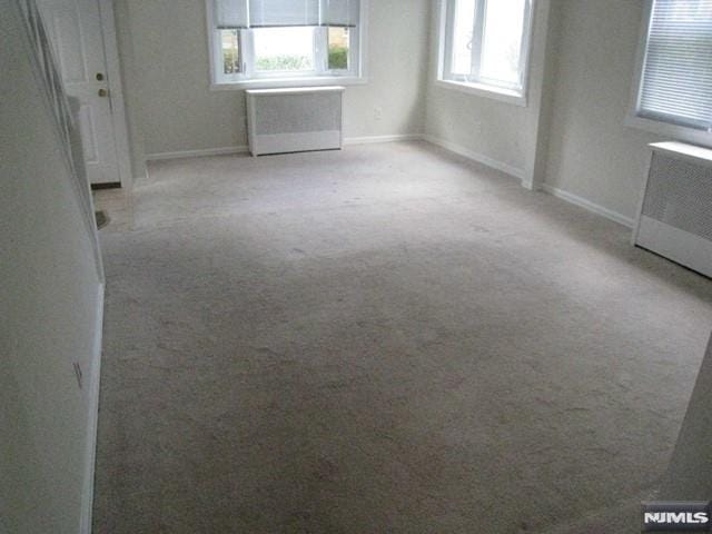 unfurnished room with a wealth of natural light, light carpet, and radiator heating unit