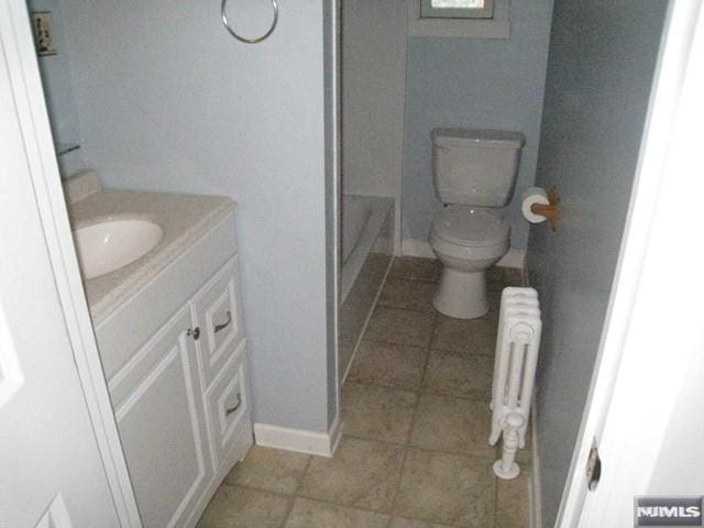 bathroom featuring radiator heating unit, vanity, a tub to relax in, and toilet