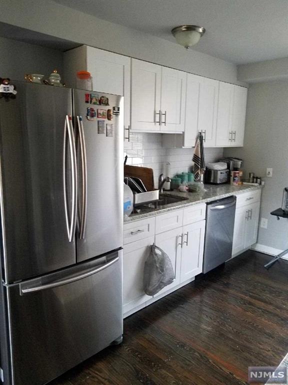 kitchen with sink, dark wood-type flooring, stainless steel appliances, tasteful backsplash, and white cabinets