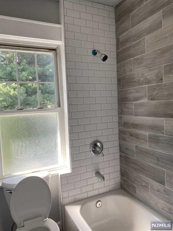 bathroom with toilet and tiled shower / bath