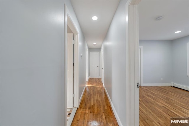 hallway with baseboard heating and light hardwood / wood-style flooring