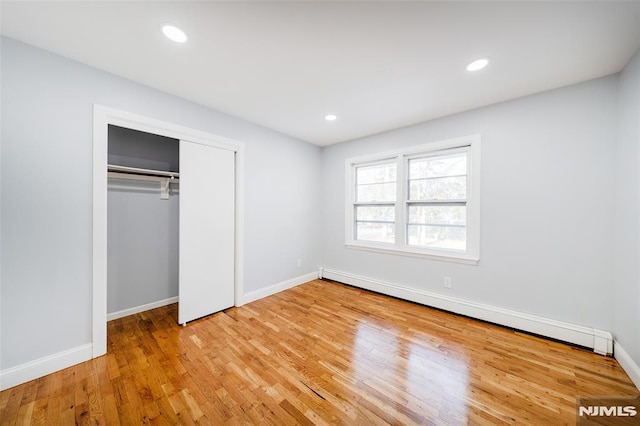 unfurnished bedroom with a closet, light hardwood / wood-style flooring, and a baseboard radiator