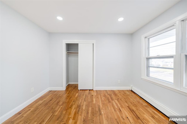 unfurnished bedroom featuring multiple windows, a closet, a baseboard radiator, and light hardwood / wood-style floors