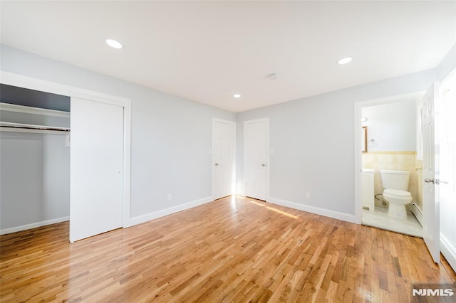 unfurnished bedroom with ensuite bathroom, a closet, a baseboard radiator, and light hardwood / wood-style flooring