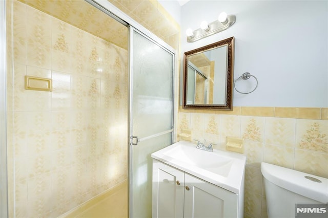 bathroom featuring vanity, a shower with shower door, tile walls, and toilet