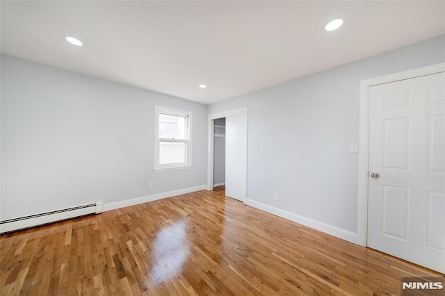 unfurnished bedroom with hardwood / wood-style flooring and a baseboard heating unit