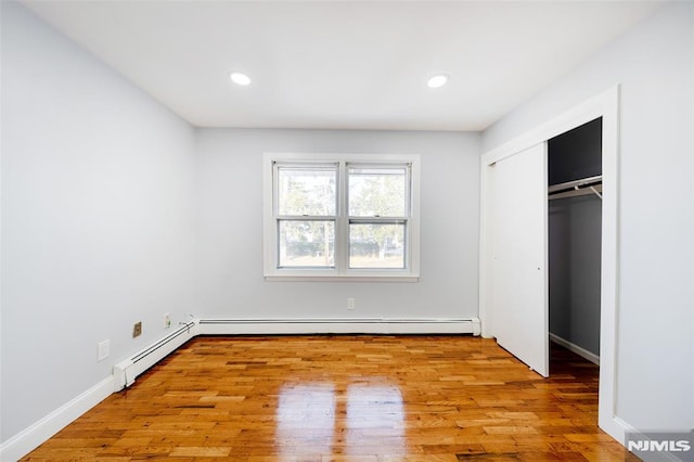 unfurnished bedroom featuring light hardwood / wood-style floors, a baseboard radiator, and a closet