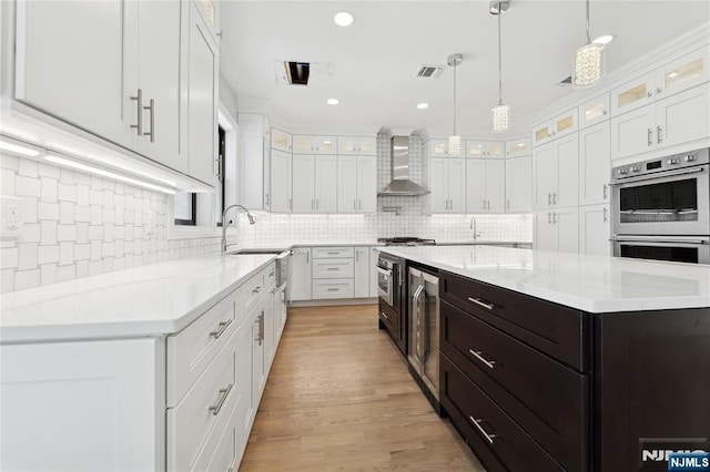 kitchen with white cabinets, double oven, a kitchen island, and wall chimney range hood