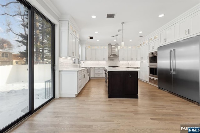 kitchen featuring appliances with stainless steel finishes, pendant lighting, white cabinets, a center island, and wall chimney exhaust hood