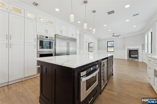 kitchen with crown molding, built in refrigerator, white cabinetry, double wall oven, and a kitchen island