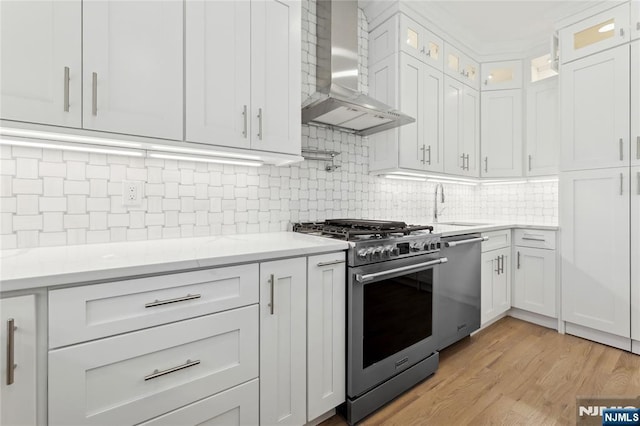 kitchen with white cabinetry, sink, dishwashing machine, high end range, and wall chimney range hood