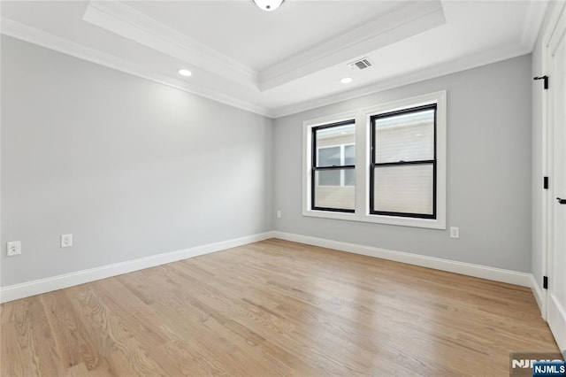 unfurnished room featuring a raised ceiling, crown molding, and light wood-type flooring