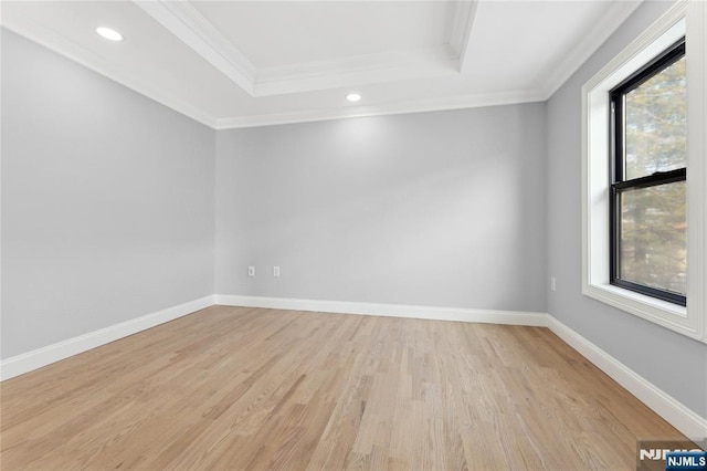 empty room with a raised ceiling, ornamental molding, and light wood-type flooring