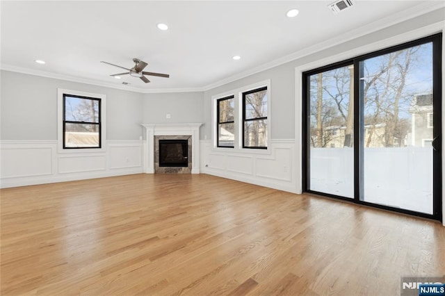 unfurnished living room with a high end fireplace, ornamental molding, ceiling fan, and light wood-type flooring