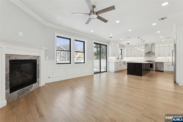 unfurnished living room with sink, crown molding, ceiling fan, a high end fireplace, and light wood-type flooring