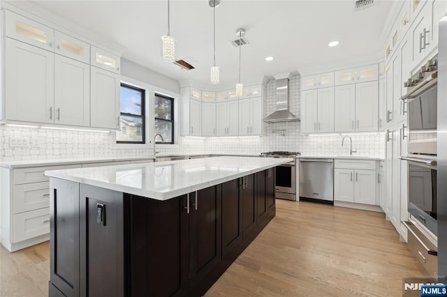 kitchen with wall chimney exhaust hood, white cabinetry, decorative light fixtures, a center island, and appliances with stainless steel finishes