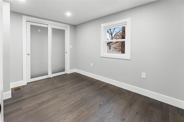 unfurnished bedroom with dark wood-style flooring, a closet, visible vents, and baseboards