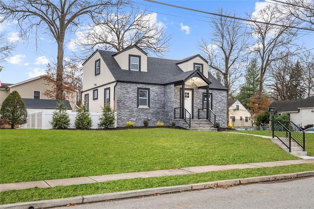 view of front of property with stone siding, a shingled roof, fence, and a front yard