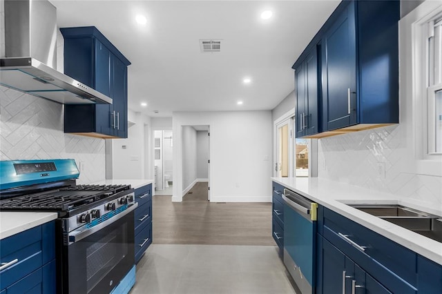 kitchen with light countertops, stainless steel gas stove, wall chimney range hood, blue cabinets, and dishwasher