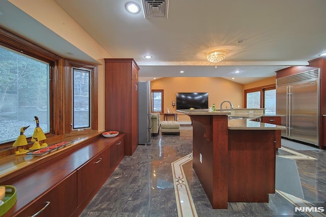 kitchen featuring a breakfast bar area, stainless steel built in fridge, a center island with sink, and sink