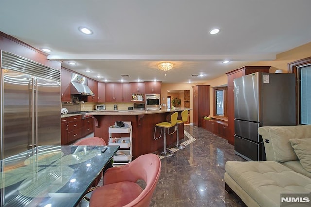 kitchen featuring appliances with stainless steel finishes, a kitchen breakfast bar, sink, wall chimney range hood, and a large island