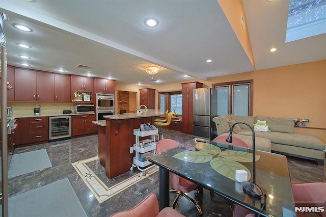 kitchen featuring sink, wine cooler, an island with sink, appliances with stainless steel finishes, and a breakfast bar area