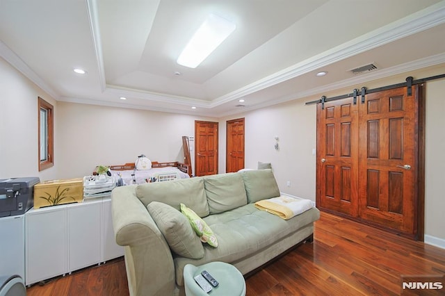 living room with dark wood-type flooring, a barn door, a tray ceiling, and ornamental molding