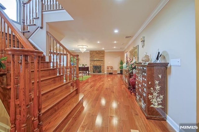 stairs with hardwood / wood-style flooring, a stone fireplace, and ornamental molding