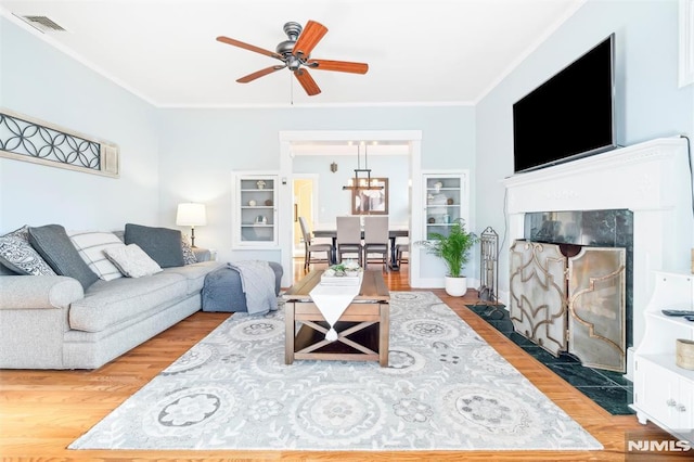 living room featuring a fireplace, light hardwood / wood-style floors, ceiling fan, and crown molding