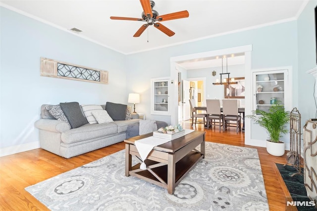 living room featuring ceiling fan with notable chandelier, wood-type flooring, and ornamental molding