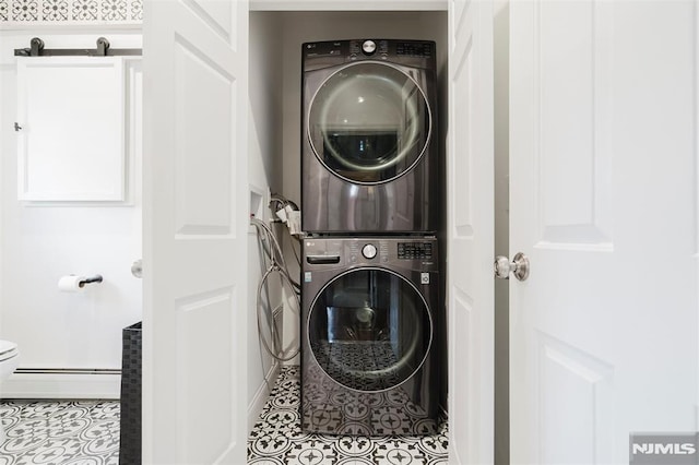 clothes washing area featuring baseboard heating, light tile patterned floors, and stacked washing maching and dryer