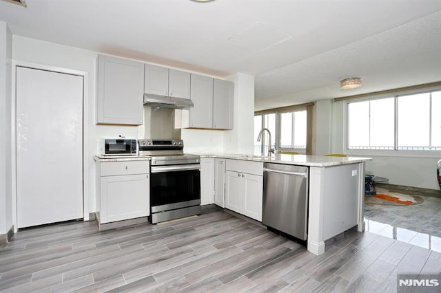 kitchen with kitchen peninsula, light stone counters, stainless steel appliances, sink, and white cabinetry