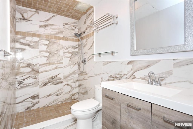 bathroom featuring vanity, decorative backsplash, toilet, tiled shower, and tile walls