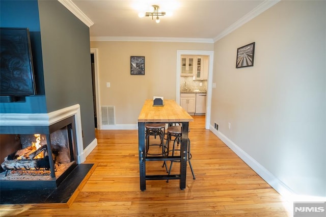 dining room with light hardwood / wood-style floors, a multi sided fireplace, and ornamental molding