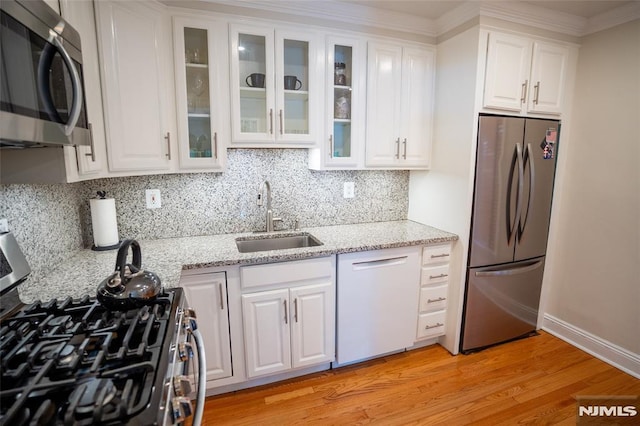 kitchen featuring light stone countertops, light wood-type flooring, stainless steel appliances, sink, and white cabinets