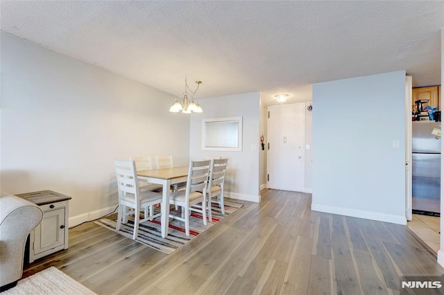 dining space with light hardwood / wood-style flooring, a chandelier, and a textured ceiling