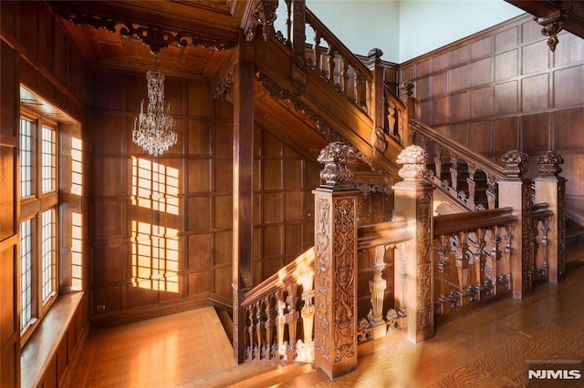 stairway with a chandelier, wood-type flooring, a towering ceiling, and wood walls