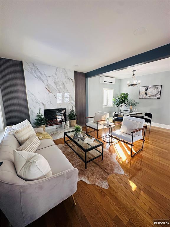 living room with a high end fireplace, an inviting chandelier, an AC wall unit, light wood-type flooring, and beam ceiling