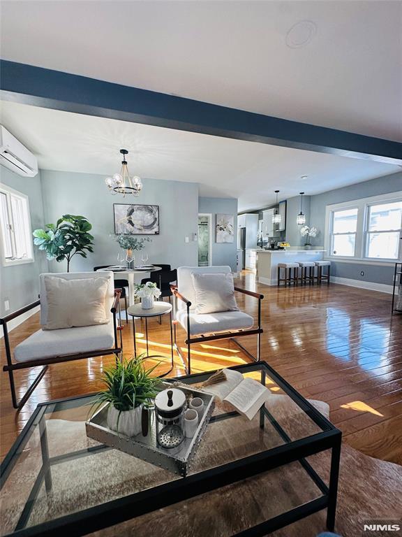 living room featuring a wall mounted AC, hardwood / wood-style floors, beamed ceiling, and a chandelier