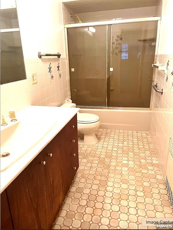 full bathroom featuring vanity, combined bath / shower with glass door, tile patterned flooring, toilet, and tile walls