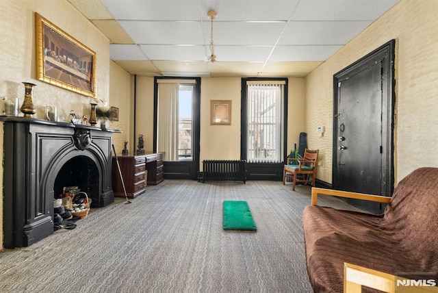 living area with carpet flooring, radiator heating unit, and a paneled ceiling