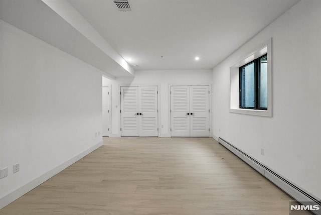 unfurnished bedroom with two closets, light hardwood / wood-style flooring, and baseboard heating