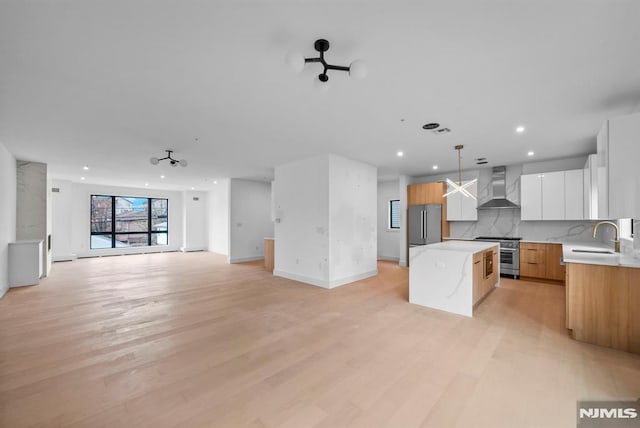 kitchen featuring a center island, white cabinets, wall chimney exhaust hood, decorative light fixtures, and stainless steel appliances