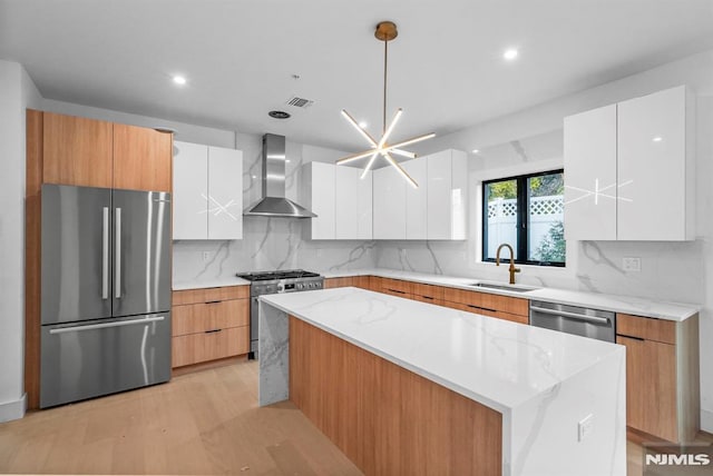 kitchen with white cabinets, sink, stainless steel appliances, and wall chimney range hood