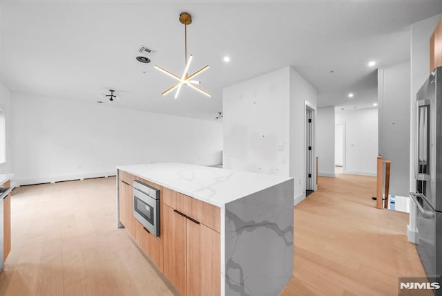 kitchen with light stone counters, a kitchen island, stainless steel appliances, and light wood-type flooring