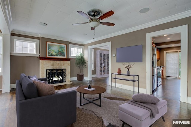 living room with hardwood / wood-style flooring, ceiling fan, ornamental molding, and a tiled fireplace