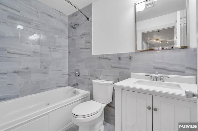 full bathroom with vanity, tiled shower / bath combo, toilet, and tile walls