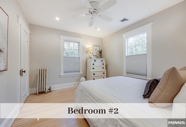 bedroom with radiator, ceiling fan, light hardwood / wood-style floors, and multiple windows